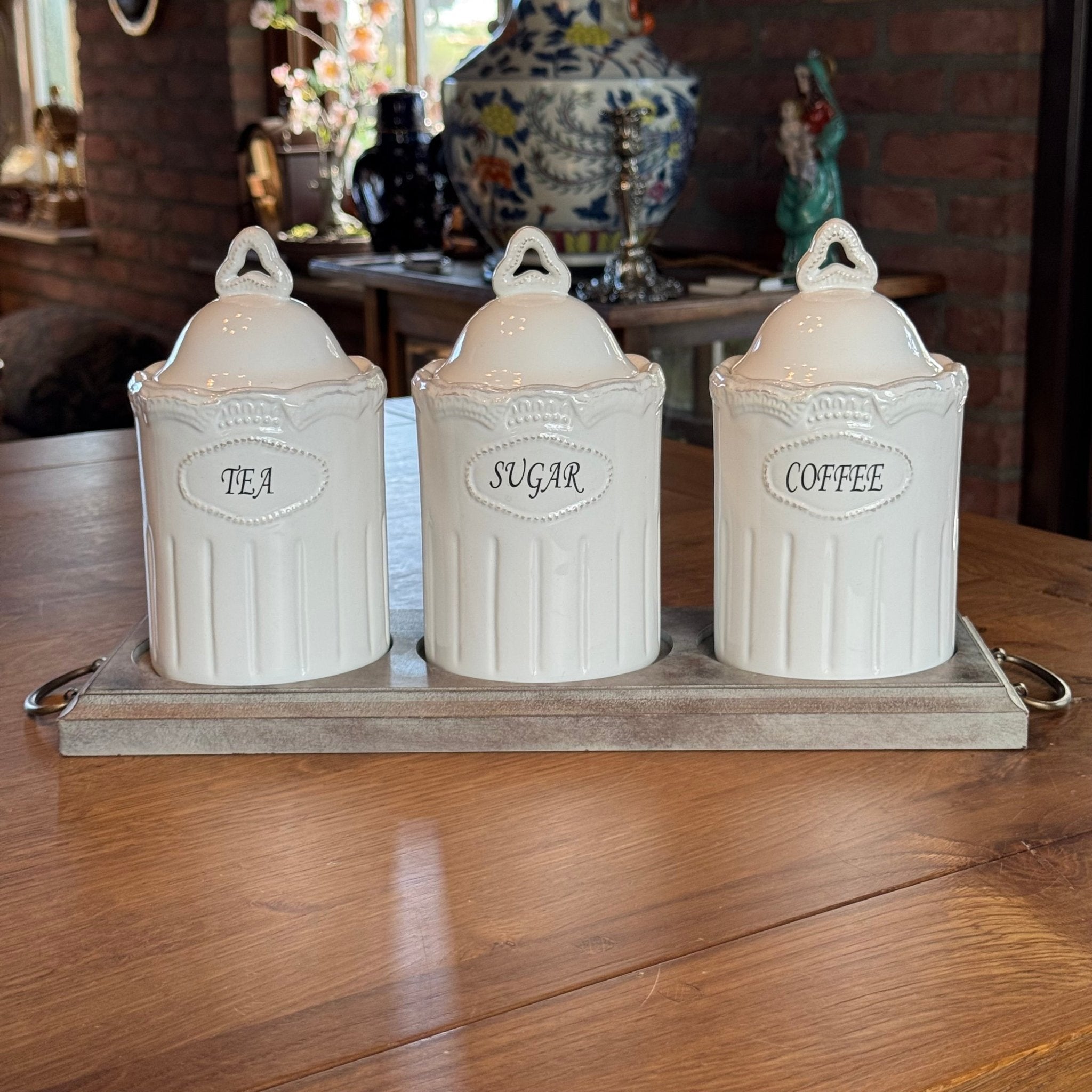 Driedelige voorraadpottenset van wit keramiek met Tea Sugar Coffee labels op houten tray in landelijke stijl