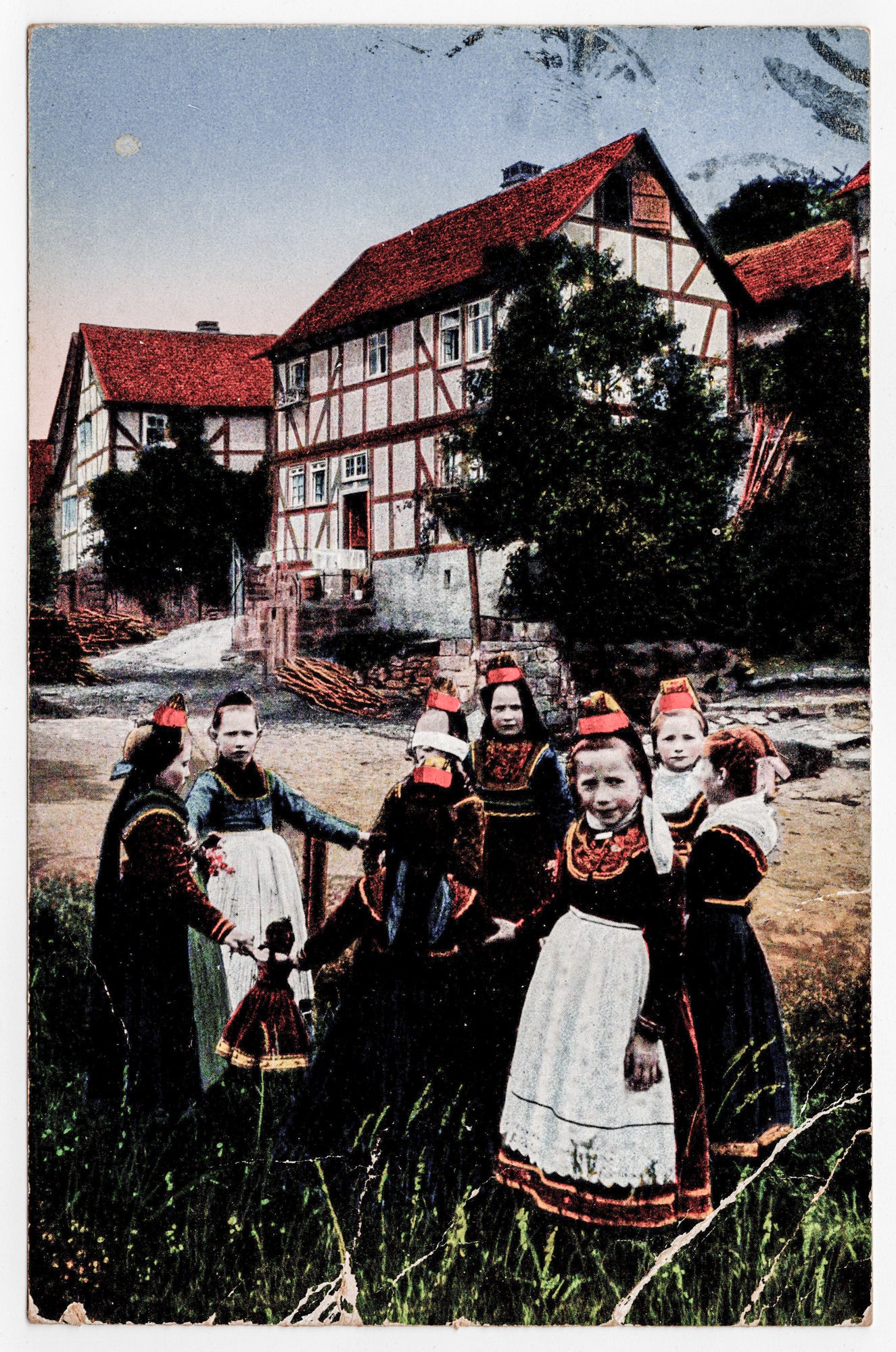 Duitse ansichtkaart 1921, ingekleurde fotolithografie Hessische meisjes in Schwalmer klederdracht met rode Stülpchen voor vakwerkhuis, uitgave Gustav Mandt Lauterbach